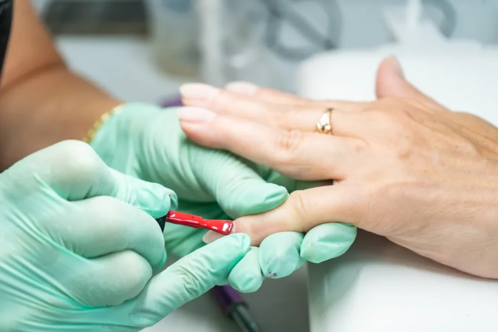Zbliżenie na nakładanie czerwonego lakieru na paznokieć podczas manicure