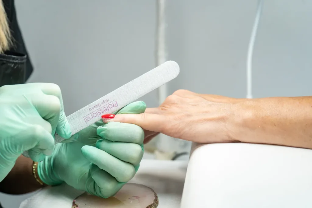 Kosmetyczka w rękawiczkach pilnikuje paznokcie klientki podczas manicure